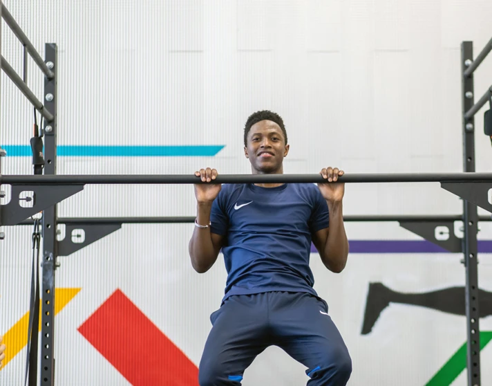 Student mid-pull-up on gym rig with colourful wall graphics behind. Student mid-pull-up on gym rig with colourful wall graphics behind.